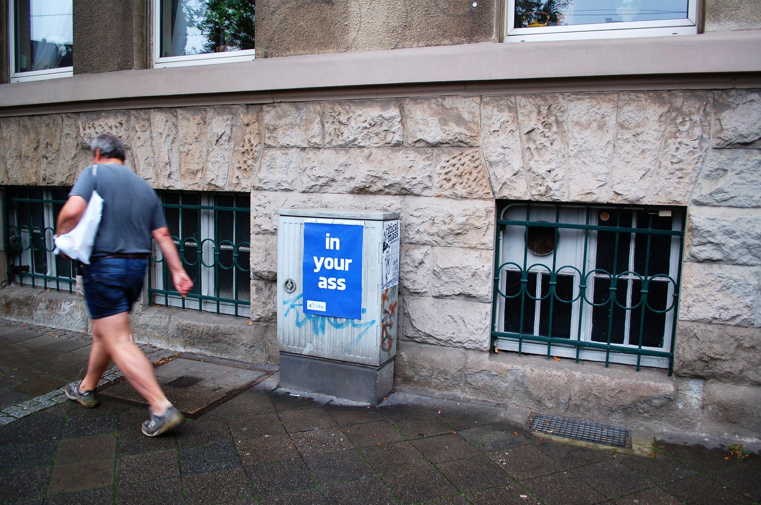 transprivacy — Filippo Minelli's blue 'in your ass' poster on a stone facade